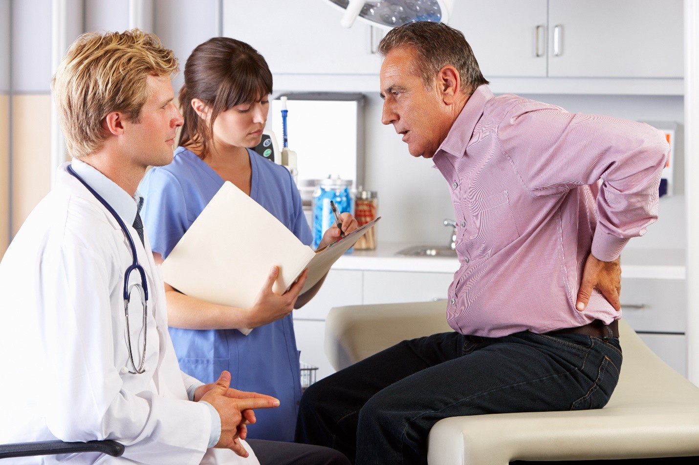 A doctor and a nurse examining a patient who is holding his lower back in pain