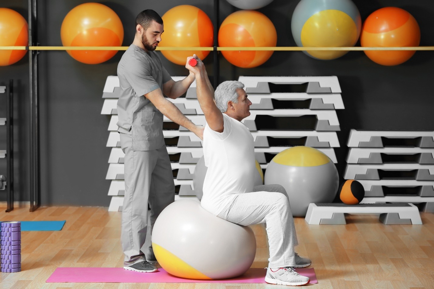 Physiotherapist assisting an elderly patient with stability exercises on a large exercise ball