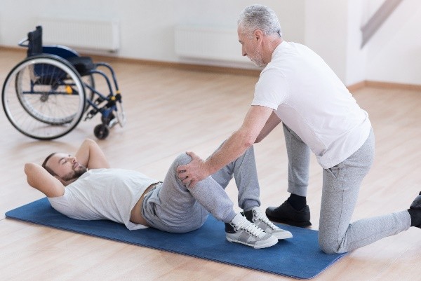 Physiotherapist assisting a patient with leg exercises on a mat
