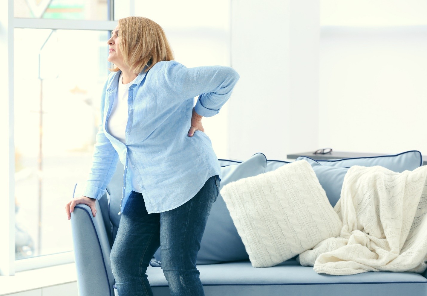 Woman standing by a sofa holding her lower back in pain